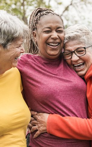 Happy multiracial senior women having fun together outdoor - Elderly generation people hugging each other at park